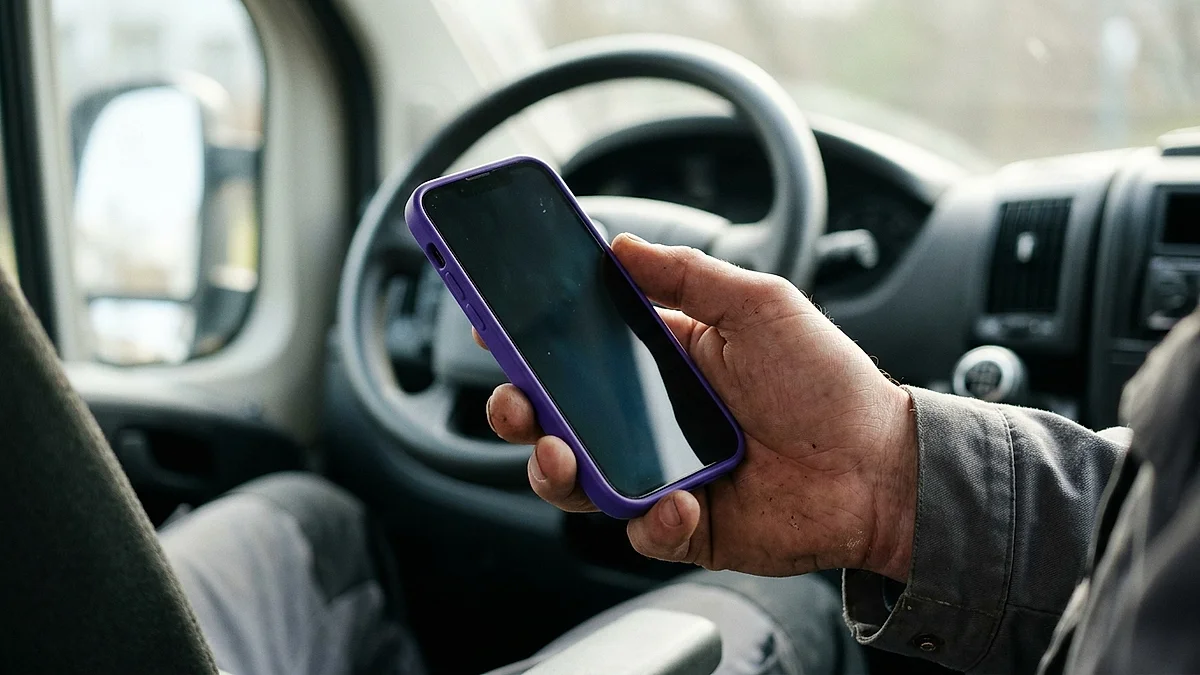 Handwerker hält im Transporter sein Smartphone in der Hand